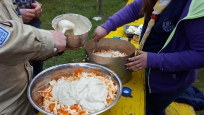 Essensausgabe im Zeltlager mit zwei Kochtöpfen auf einem Holztisch und Händen, die umrühren