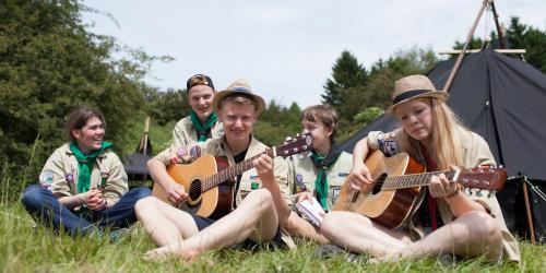 Eine Gruppe Jugendlicher sitzt mit Gitarre vor einem Zelt