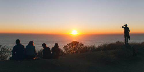 Kleine Menschengruppe vor Sonnenuntergang an einer Steilküste
