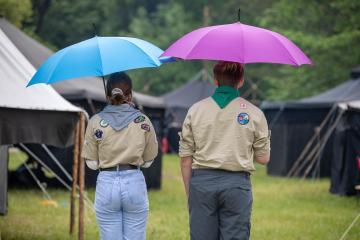 Leiterin und Pfadi laufen Richtung Lager. Beide haben einen Regenschirm aufgespannt. 