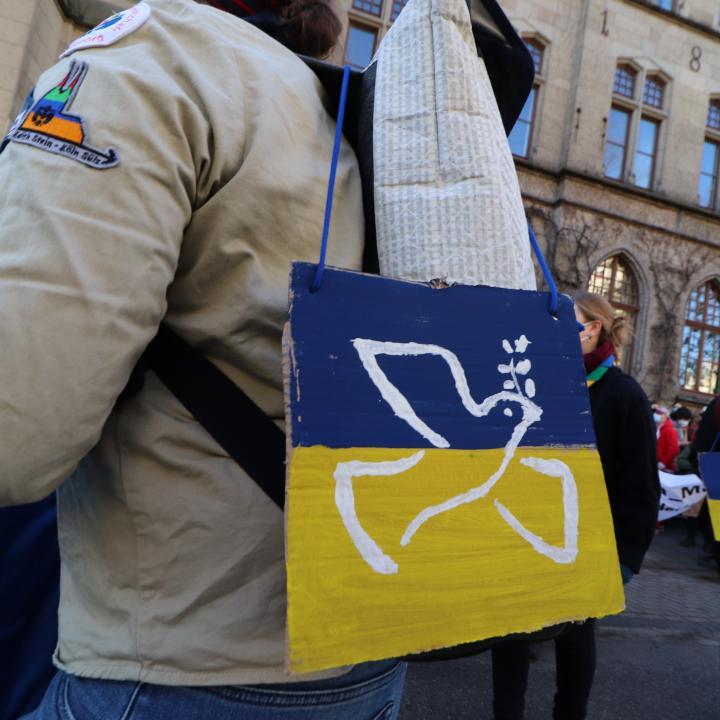 Person in DPSG-Kluft mit einem blau-gelben Schild mit einer Friedenstaube bei einer Friedensdemonstration in Köln